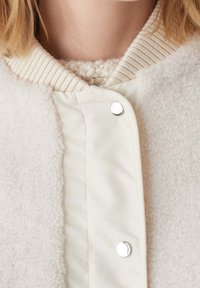 Biała kurtka bombka z puszystej, teksturowanej tkaniny z gładką podszewką, prążkowanym kołnierzem i zapięciem na napy.