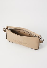 Beige nahkalaukku vetoketjulla, jossa on kohokuvioitu "Calvin Klein Jeans" -logo, hopeiset yksityiskohdat ja tyylikäs, minimalistinen muotoilu.