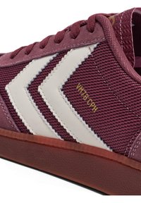 Bordó sportcipők fehér farkasfog mintával, texturált anyaggal és velúr díszítéssel. Áttetsző gumitalppal és arany színű márkajelzéssel rendelkeznek.