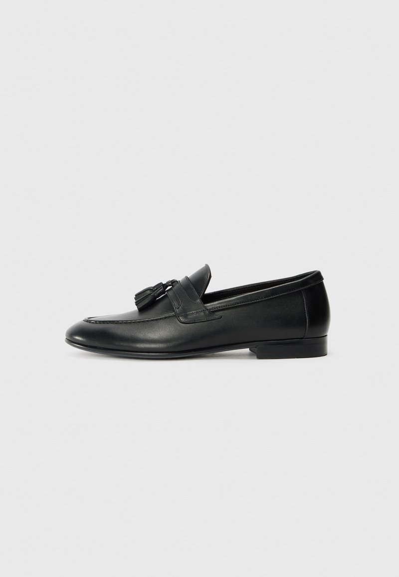 Black leather loafers with a smooth texture, rounded toe, and decorative tassels on the front. Low, flat heel and minimalist design.