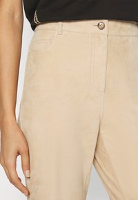 Μπεζ σουέτ παντελόνι με απαλή υφή, διαθέτει κλείσιμο με κουμπί μπροστά, πλαινές τσέπες και ορατές λεπτομέρειες ραφής.