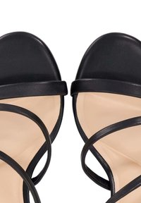 Zwarte leren sandalen met een gladde textuur, voorzien van dunne gekruiste banden en een zachte beige binnenzool. Open teen ontwerp.