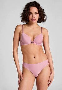 Sujetador rosa claro y braguita a juego, tela suave, tirantes ajustables, soporte con aro y un pequeño broche decorativo en la parte delantera.