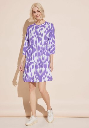 Violetti ja valkoinen kuviollinen mekko, jossa on kolmanneksen hihat, kerroksellinen helma, pyöreä pääntie, yhdistetty valkoisten tennareiden kanssa. Sileä kankaan pinta.
