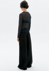 Transparente schwarze Langarmbluse mit horizontalen Streifen, kombiniert mit lockeren schwarzen Weitbeinhosen mit hoher Taille und Gesäßtaschen.