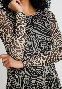 Genomskinlig topp med en blandning av djurmönster i beige och svart, med långa ärmar och rund halsringning. Slät textur genom hela plagget.