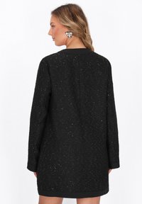 Abito nero con textures e motivo tessuto, caratterizzato da una vestibilità regolare e maniche lunghe. Completato da un orlo nero a contrasto.