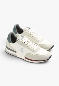 Sneaker sportive bianche con accenti grigi e teal, dotate di una parte superiore testurizzata, un logo a forma di teschio prominente e una suola imbottita con battistrada a motivo.