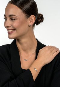 Silver infinity necklace and bracelet, featuring a sleek design with interlocking loops, worn on a model against a white background.