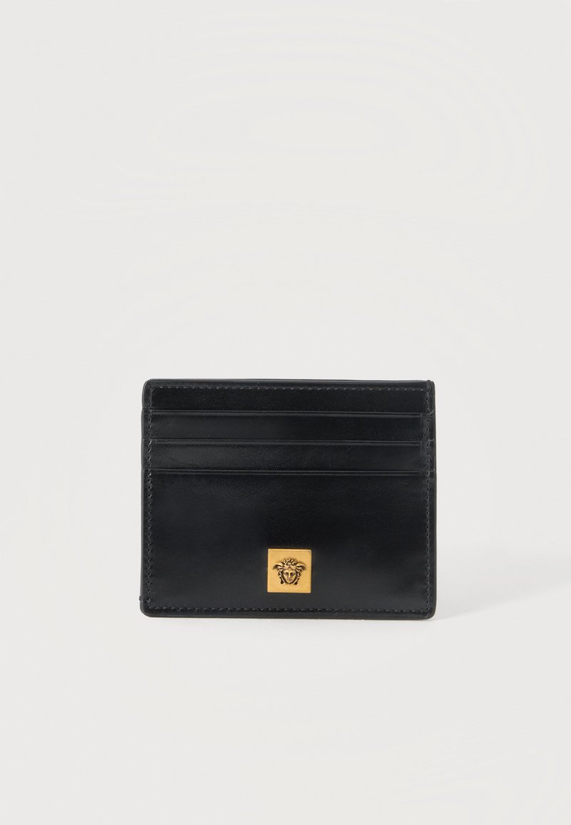 Porte-cartes en cuir noir avec quatre emplacements pour cartes et un emblème doré en forme de tête de Méduse au centre en bas.