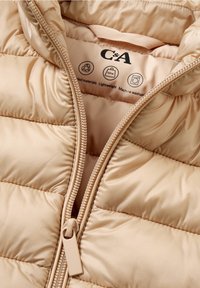 Beżowa kurtka puchowa o gładkiej teksturze. Posiada zamek błyskawiczny z przodu, pikowany design oraz symbole pielęgnacji na wewnętrznej podszewce. Lekka i nadająca się do prania w pralce.