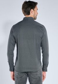 Schwarz-weiße, gemusterte Langarmbluse mit Kentkragen und verstellbaren Manschetten, aus leichtem Stoff gefertigt.