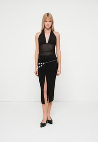 Black halter top with sheer fabric, paired with a fitted black skirt featuring a side slit and silver star accents on a chain belt.