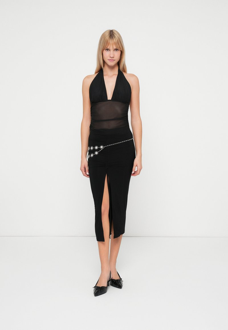 Black halter top with sheer fabric, paired with a fitted black skirt featuring a side slit and silver star accents on a chain belt.