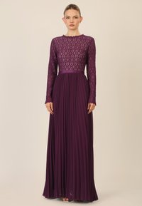 Pitkällä violetti mekolla, jossa on pitsinen vartalo-osa, pitkät hihat, aaltoileva pääntie ja liehukehame. Valmistettu tekstuuri materiaaleista, elegantti muotoilu.