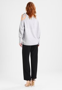 Grå stickad tröja med utskärning vid axlarna och en rosettdetalj, ihop med svarta vida byxor och beiga högklackade skor.