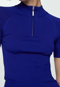 Prążkowany, jaskrawo niebieski top z krótkimi rękawami i wysokim kołnierzem z srebrnym zamkiem przy szyi. Tkanina o fakturze, dopasowany fason.