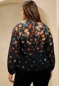 Schwarze durchsichtige Bluse mit lebhaften Blumenmustern, langen Puffärmeln und einem Schlüsselloch-Ausschnitt auf der Rückseite. Die glatte Textur ergänzt das Design.