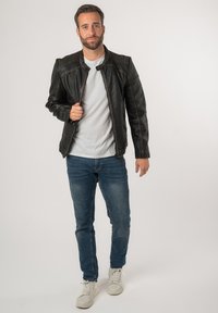 Giubbotto di pelle nera con dettagli testurizzati sulle spalle, chiusura a zip frontale e cucitura a contrasto. Abbinato a una camicia bianca e jeans blu.