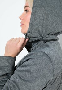 Grå huvtröja i texturerad tyg, med dragsko på huvan och en dragkedjeficka på sidan.