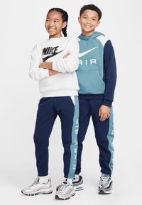 Dve deti nosia zladené športové oblečenie. Jedno má biele mikinu s čiernym logom; to druhé má na sebe modrú mikinu. Obe majú na sebe námornícke jogger nohavice.