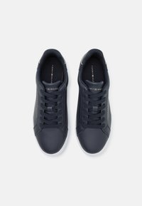 Baskets en cuir marine avec semelle blanche, lacets plats et un logo sur la languette. Présente une texture lisse et un design minimaliste.