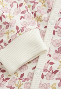 Blumenmuster-Cardigan in Creme, mit pinken und goldenen Blumen. Gerippte Bündchen und Knopfverschluss mit weißen Knöpfen. Weicher Stoff.