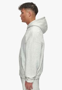 Haut à capuche gris clair avec une grande poche kangourou, cordon de serrage à capuche et poignets côtelés. Fabriqué en tissu doux et texturé, offrant une coupe décontractée.