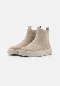 Beige Wildleder-Ankle Boots mit elastischen seitlichen Einsätzen, runder Zehenpartie und einer dicken, strukturierten Sohle für besseren Halt. Doppelte Zuglaschen für ein einfaches Anziehen.
