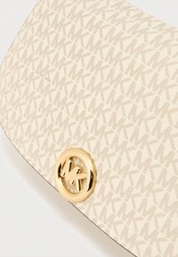 Μπεζ δερμάτινο τσαντάκι χειρός με επαναλαμβανόμενο μοτίβο 'K', διακοσμημένο με χρυσό κυκλικό λογότυπο. Ομαλή υφή με κομψό σχεδιασμό.