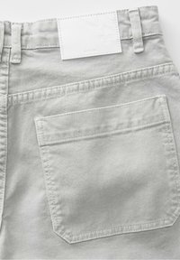Jean en denim gris clair en gros plan montrant la poche arrière, les passants de ceinture et une étiquette de marque rectangulaire blanche cousue au-dessus de la poche.