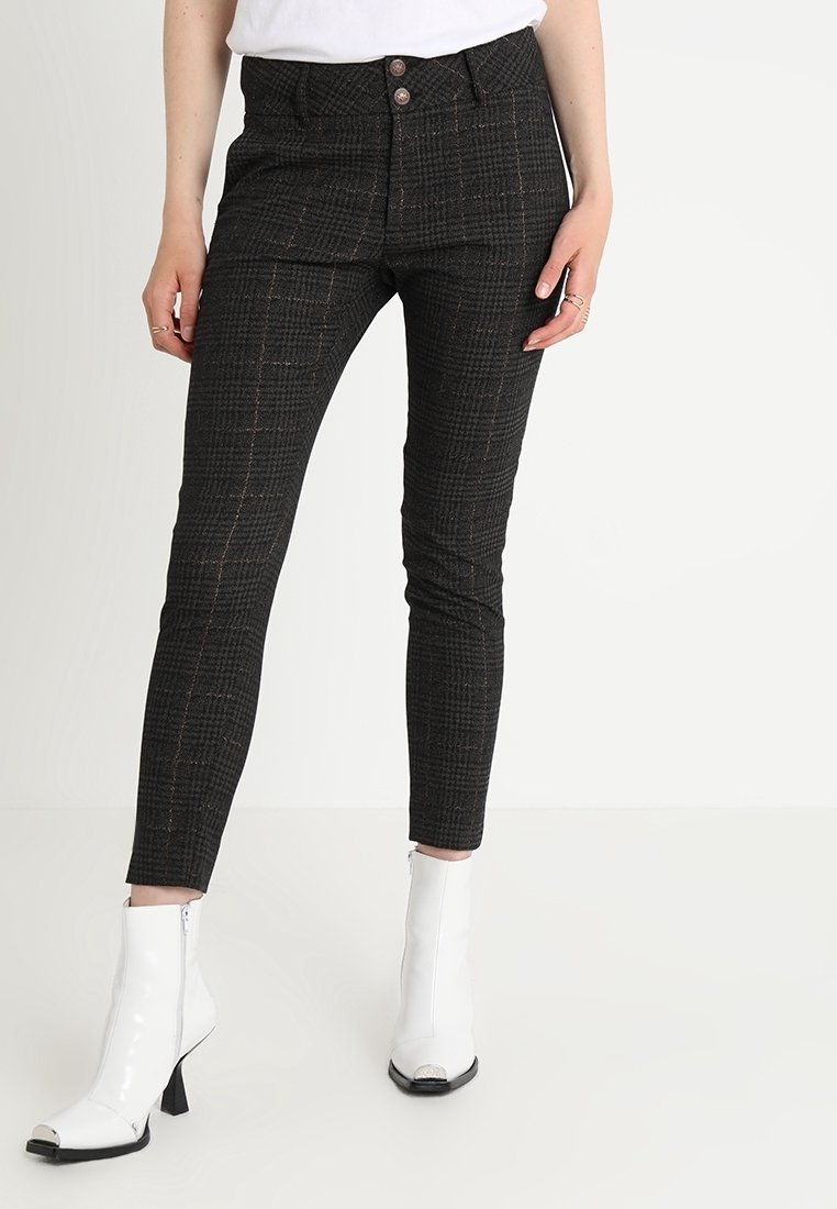 Pantalon slim fit à carreaux foncés avec des boutons sur le devant, porté avec des bottines blanches à talons et un top blanc rentré.