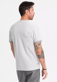 Lys grå bomulds t-shirt med korte ærmer og en kontrastfarvet grå kant. Har en afslappet pasform og sideslidsdetaljer.