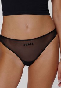 String transparent noir avec le texte "AMORE", une ceinture élastique lisse, et une couverture minimale en matériau en maille transparente.