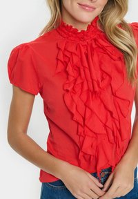 Blusa rossa con un alto colletto a balze e dettagli a balze stratificati nella parte anteriore. Maniche corte, texture liscia e taglio aderente.