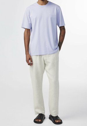 T-shirt col rond lavande clair, coupe décontractée. Associé à un pantalon en lin couleur crème et des sandales plates noires. Design simple, sans logos visibles.