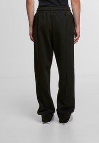 Black, tapered sweatpants with an elastic waistband, two side pockets, and a smooth fabric texture, shown from the back.