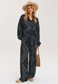 Zestaw w czarno-szary wzór bandany, składający się z szerokich spodni i luźnej bluzki, w połączeniu z beżowym kapeluszem i torbą. Miękka tekstura materiału.