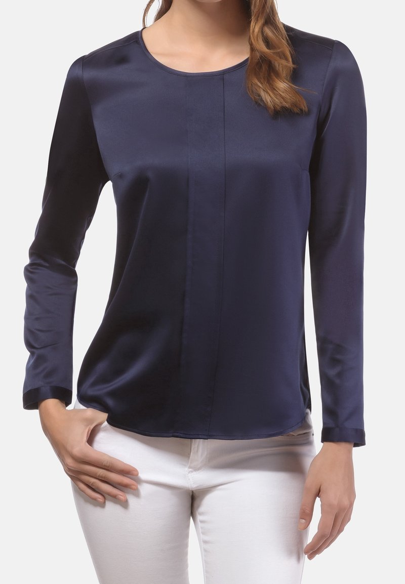 Haut long à manches en satin bleu marine avec un col rond et un détail de couture central, associé à un pantalon blanc. Texture lisse, design ajusté.