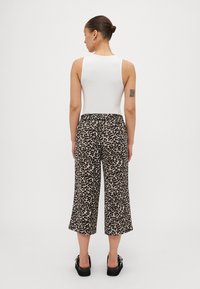 White sleeveless bodysuit paired with loose leopard-print cropped pants, featuring a stretchy waistband and a smooth texture. Black platform shoes.