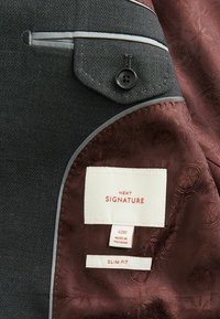 Szara kurtka o teksturowanej powierzchni i bordo satynowym podszewce. Posiada mały czarny guzik oraz metkę z napisem "NEXT SIGNATURE", dopasowany krój.