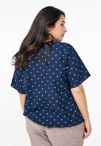 Camicia blu navy a pois con vestibilità rilassata, maniche corte e texture liscia, abbinata a pantaloni marrone chiaro.