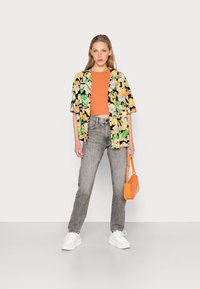 Camisa preta floral com detalhes em verde, laranja e amarelo, combinada com um top laranja e jeans cinza. Os acessórios incluem uma bolsa laranja.