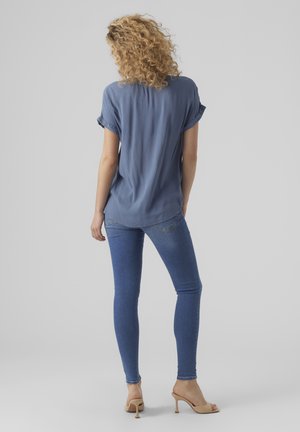 Camisa de manga corta azul claro, corte relajado, textura suave. Combinada con jeans azules de corte ajustado y tacones abiertos beige.