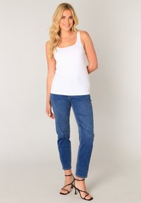 White tank top with thick straps, paired with blue high-waisted jeans and black strappy heels. Smooth fabric, fitted design.