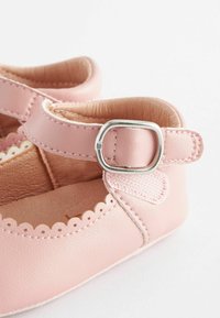 Pink leather shoe with a rounded toe, scalloped edge detail, and a silver buckle strap. Soft inner lining and textured outer finish.