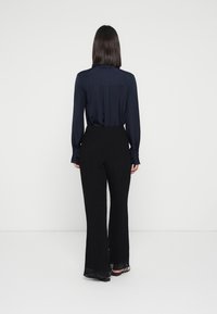 Marineblauwe zijde blouse met lange mouwen, rugplooi-detail, gecombineerd met zwarte, wijde, geplooide broeken, beide met een gladde textuur.