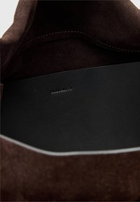 Bruine suede buitenkant met een zwart lederen interieur. Het interieur heeft reliëfbranding. Vlotte texturen en strakke lijnen overal.