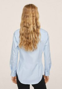 Chemise bleu clair à boutons avec manches longues, ourlet arrondi et poignets. Texture lisse avec empiècement dos droit et design structuré.