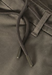 Tissu en mélange de coton de couleur vert olive, avec des cordons tressés aux accents foncés et des embouts en plastique, détails de couture visibles.